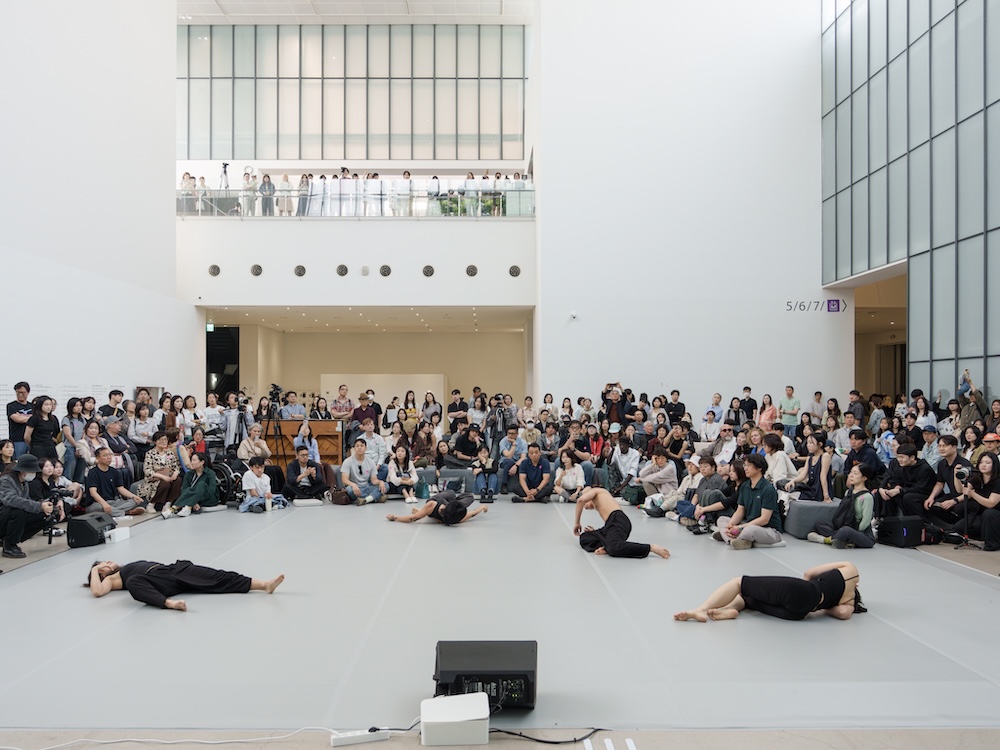 작가, 최태윤. 작품명, 내게 기대요, 부문, 벽화. 제작년도, 2025년. 벽에 실크스크린 설치, 20 ✕ 6 m. 국립현대미술관 제작지원. 두 사람이 등을 기댄 모습이 검은 선으로 그려져 있다. ‘내게 기대요’라는 문구가 한쪽에 쓰여 있다. 평화로운 표정이다.