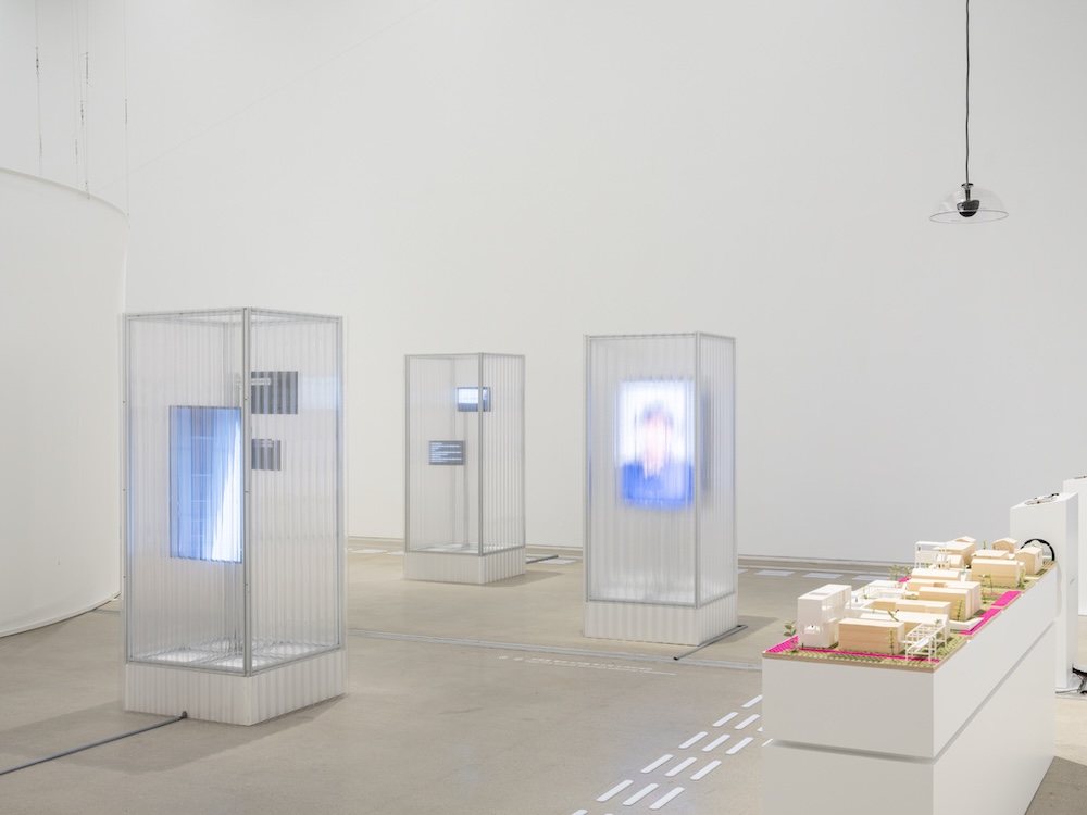 작가, 김은설. 작품명, 흐려지는 소리, 남겨진 소리. 부분, 설치. 제작년도, 2025년. 매체 및 기법, 모니터, 미디어 플레이어, 진동 스피커, 앰프, 폴리카보네이트. 규격, 가변 크기. 국립현대미술관 제작지원. 영상 스틸. 노트북 앞에 핸드폰이 놓여 있다. 노트북과, 핸드폰 화면, 이미지 하단에 각각 자막이 있다. 세 자막은 ‘밑에’로 시작되는 동일한 문장을 표시하고 있다. 하지만 속도는 달라서, 어떤 화면에는 좀더 빠르게, 다른 화면에는 좀더 느리게 자막이 나타난다.
