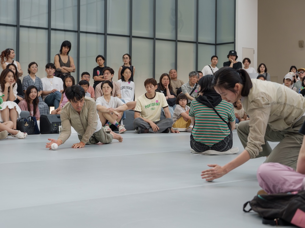 작가, 김원영. 작품명, 보철물로서 움직이기, 머신, 어포던스, 케어. 부문, 퍼포먼스. 제작년도, 2025년. 국립현대미술관 제작지원. 영상 스틸. 두 사람이 춤을 추고 있다. 한 사람은 휠체어를 타고 있다. 두 사람은 두 손을 바닥에 짚고 네 발로 움직이고 있다. 하나의 축을 중심으로 원형을 그리면서 돌고 있다.