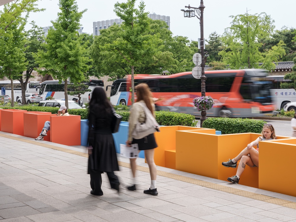 작가, 리처드 도허티. 작품명, 농인공간: 입을 맞추는 의자. 부문, 설치. 제작년도, 2025년. 매체 및 기법, 철에 도장, 가변 설치. INTG, 국립서울농학교, 다니엘 모레노 제작협력. 국립현대미술관 제작지원. 미술관 정문 계단 위에 노란색, 하늘색, 주황색 벤치가 놓여 있다. 사람들이 서로 마주보고 앉을 수 있도록 방향 지워져 있다. 벤치는 계단을 통로가 아닌 휴식공간으로 바꾼다. 미술관에 들어가려는 사람들은 모두 측면의 경사로를 이용하게 된다.