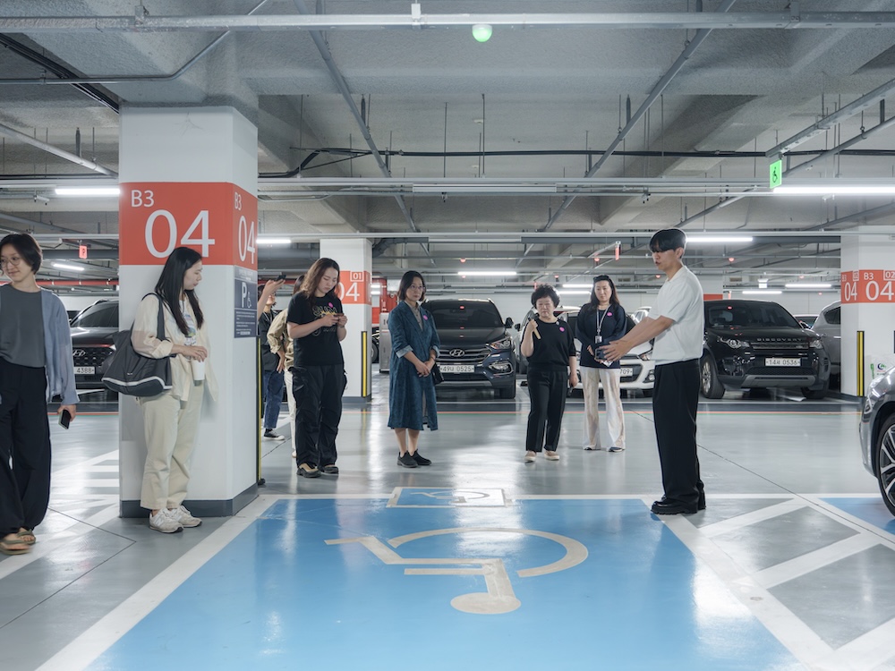 작가, 윤충근. 작품명, 격언. 부문, 설치. 제작년도, 2025년. 매체 및 기법, 아크릴에 인쇄, 가변 설치. 국립현대미술관 제작지원. 투명한 아크릴 판 안에 격언이 쓰여 있다.여느 화장실에서 볼 수 있는 것과 같은 평범한 디자인이다.  “Ey/em/eir(s)은 they/them/theirs를 줄여 말하는 성중립 대명사이다.”